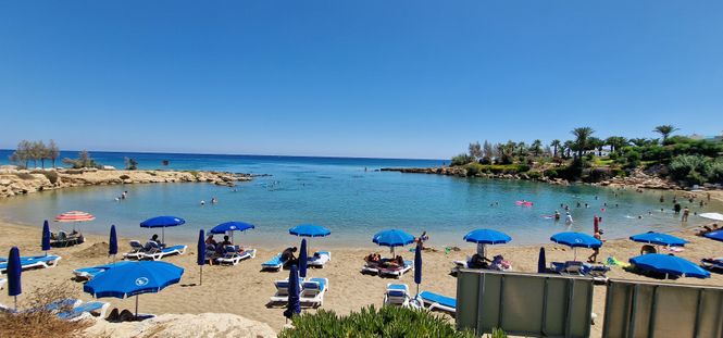 sandy beach with blue parasols and turquoise water in Protaras