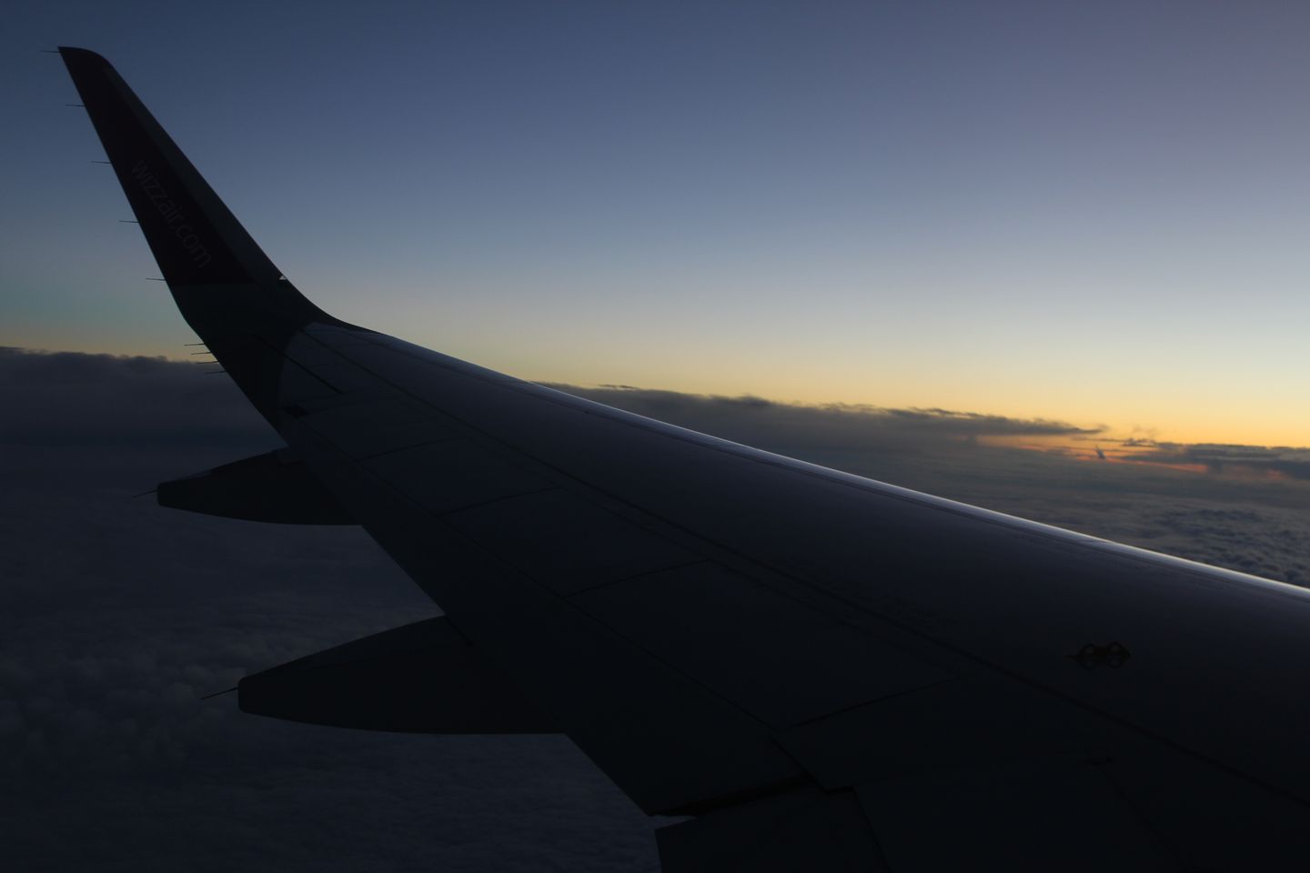 wing of a Wizz Air airplane against the sunset above clouds